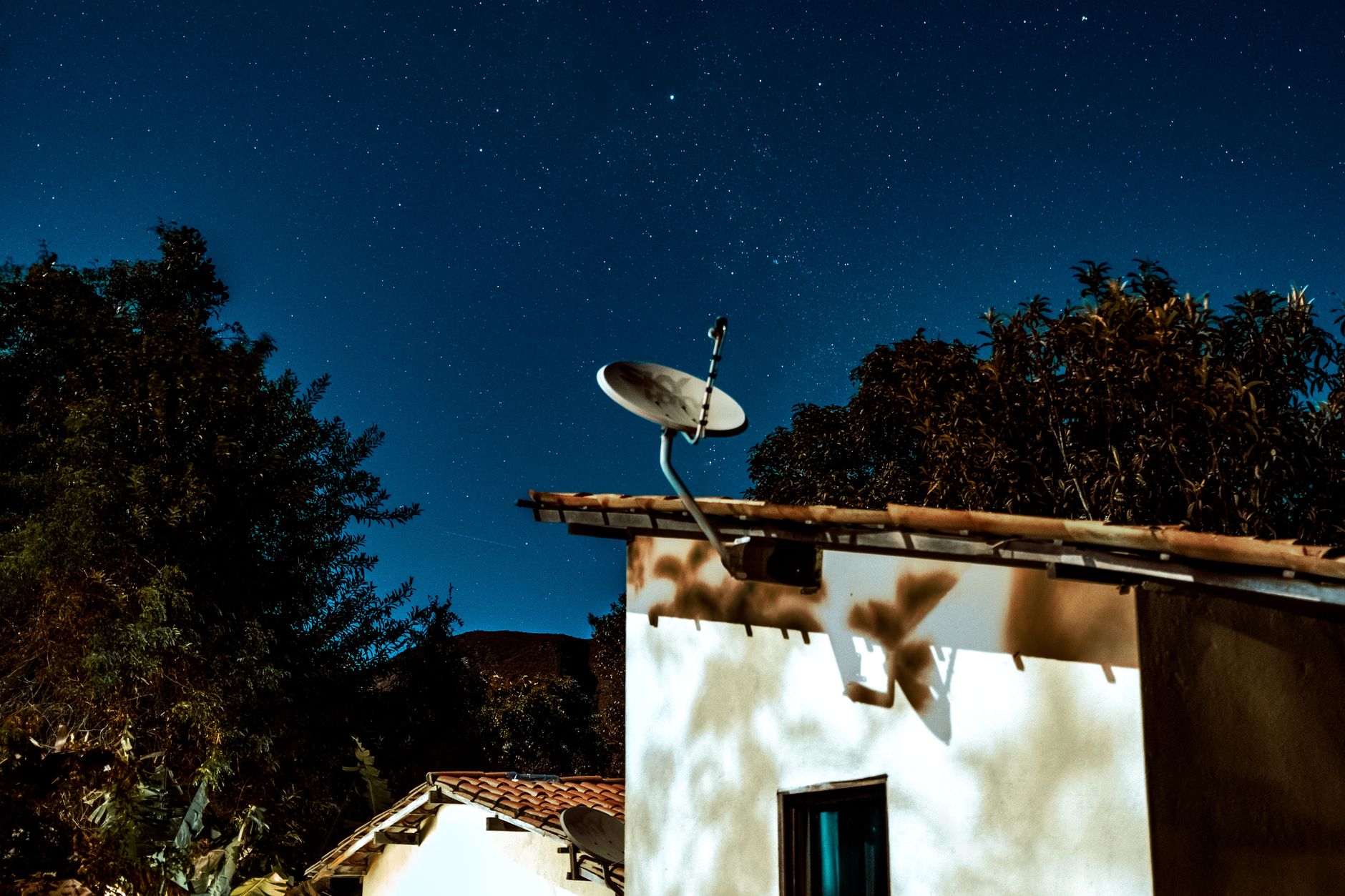 A satellite dish on a rural house beneath a starry evening sky