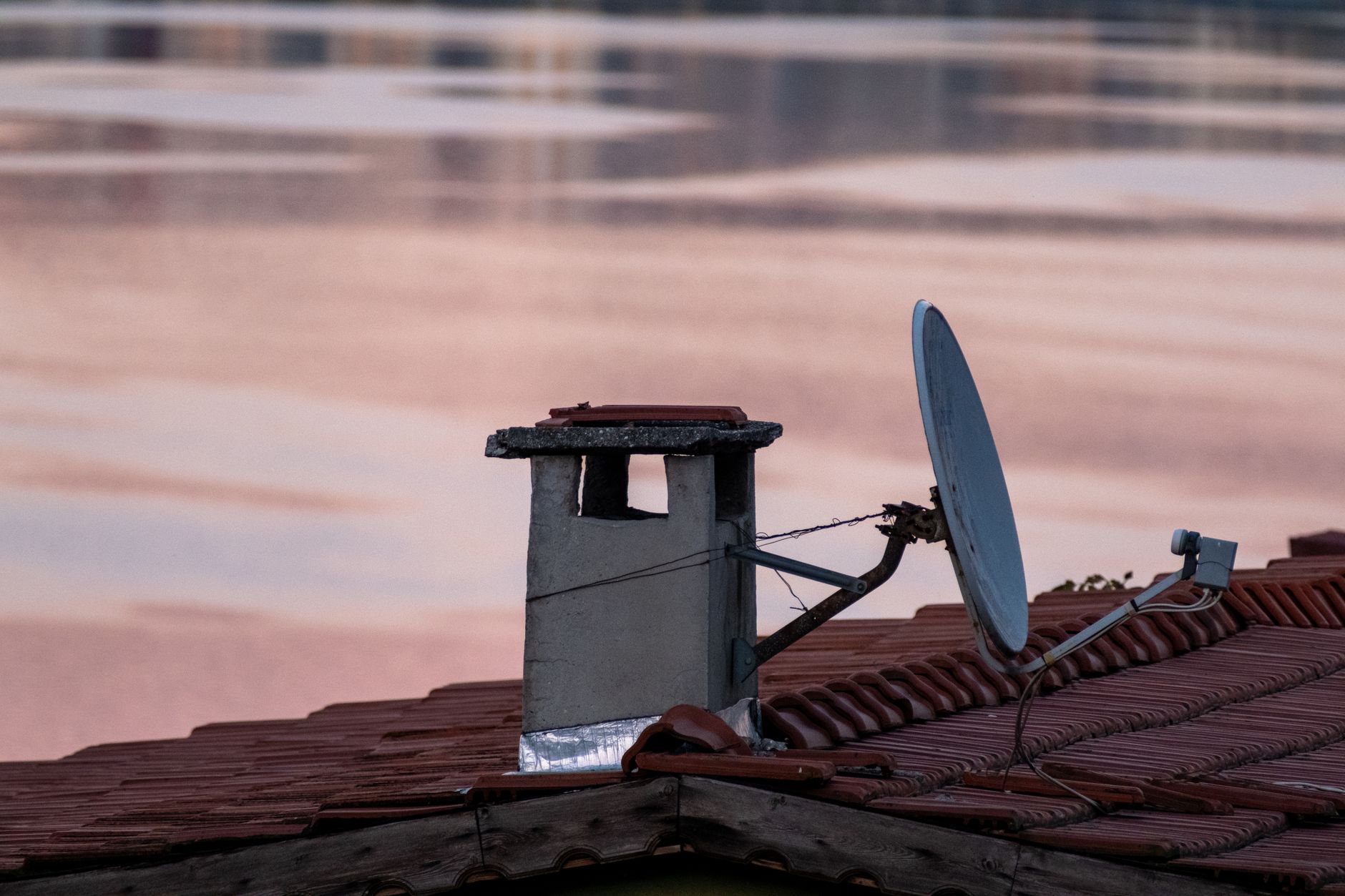 A close-up of a chimney and satellite dish on a rooftop during a serene dawn in Istanbul, Türkiye.
