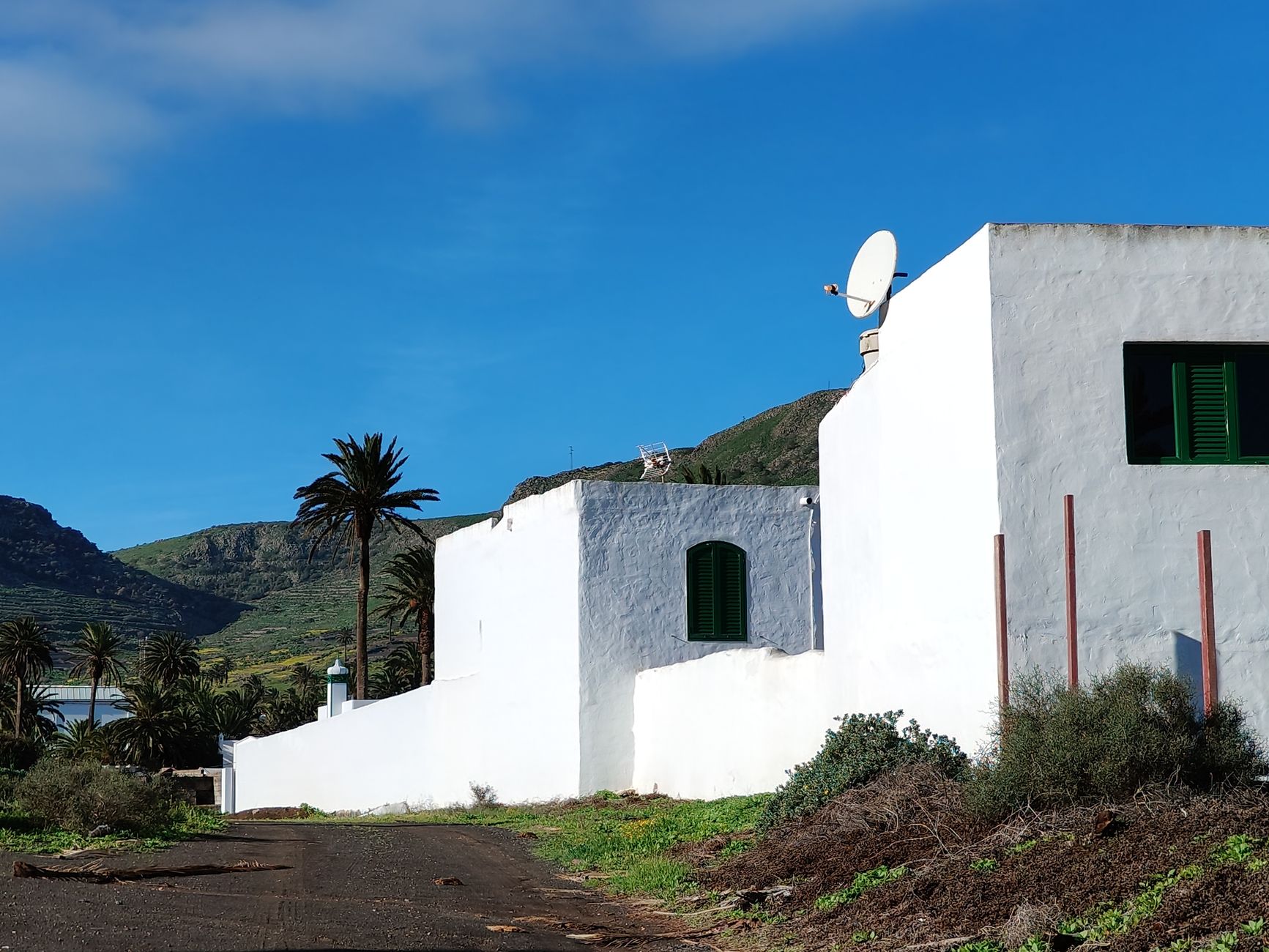 White rural building with a satellite dish beneath a clear blue sky.