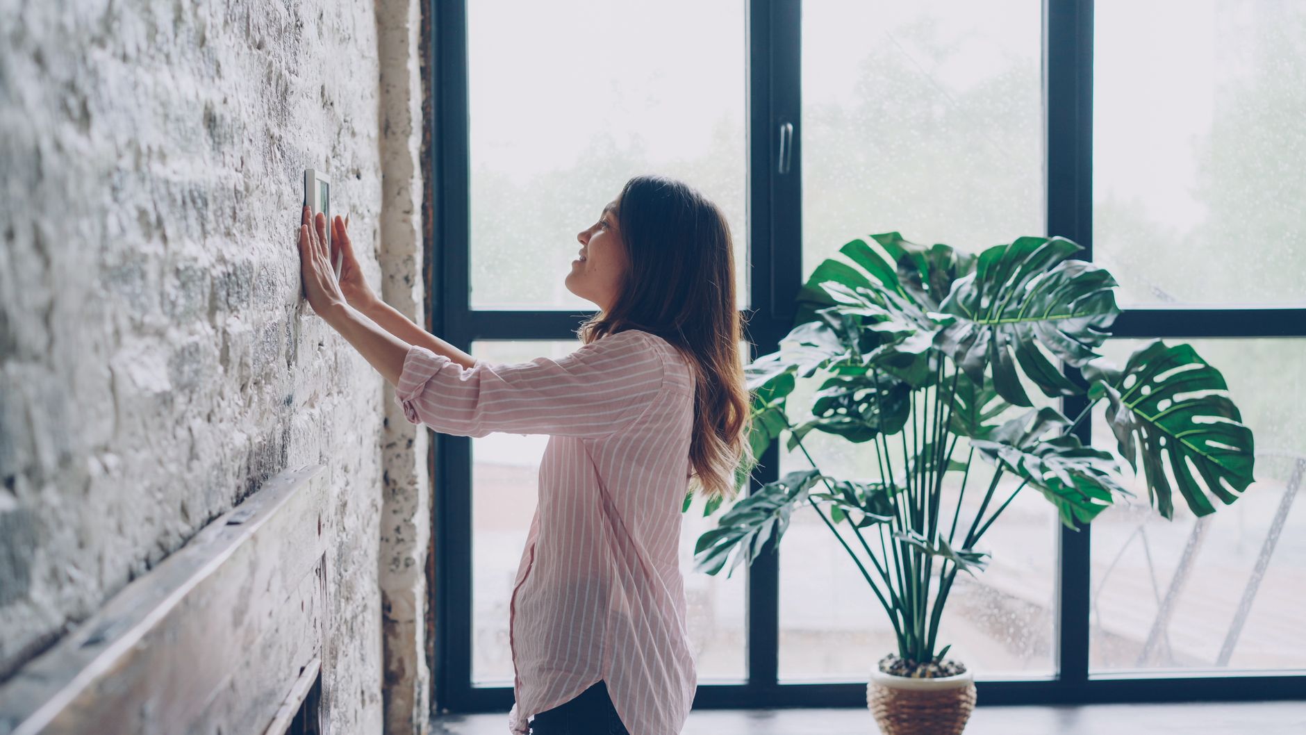 Woman adjusting a smart thermostat in a bright living room