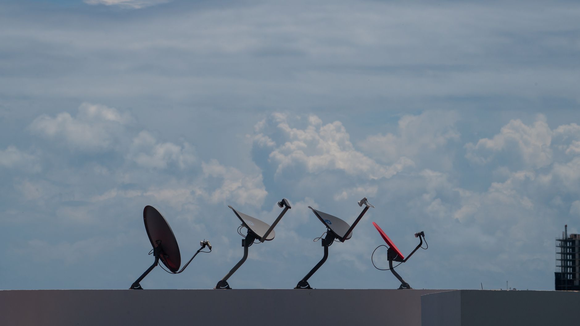 Four satellite dishes on a rooftop against a cloudy sky in Cancún, Mexico.