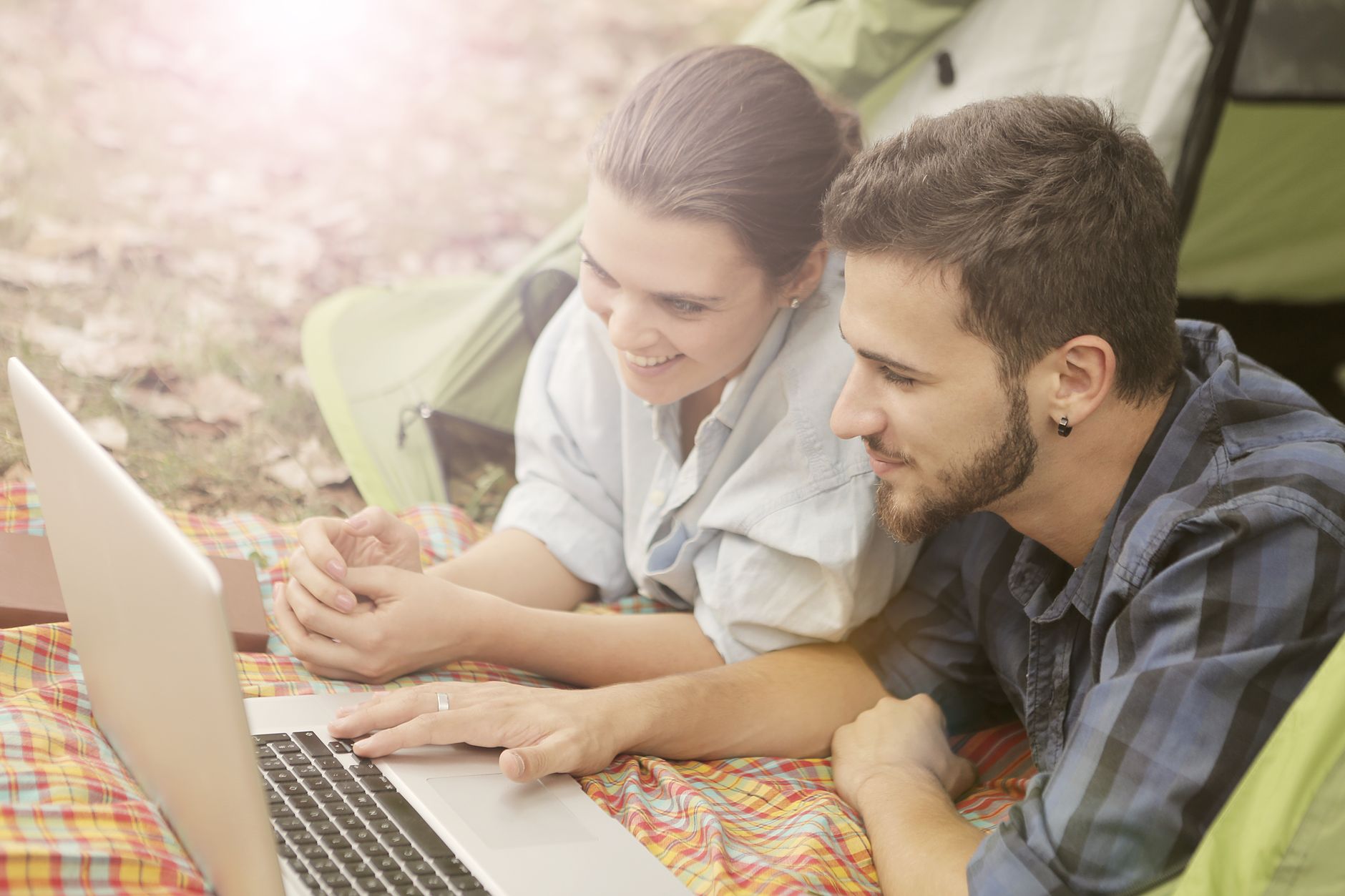 A young couple enjoying a relaxing day camping with a laptop in a sunny outdoor setting.
