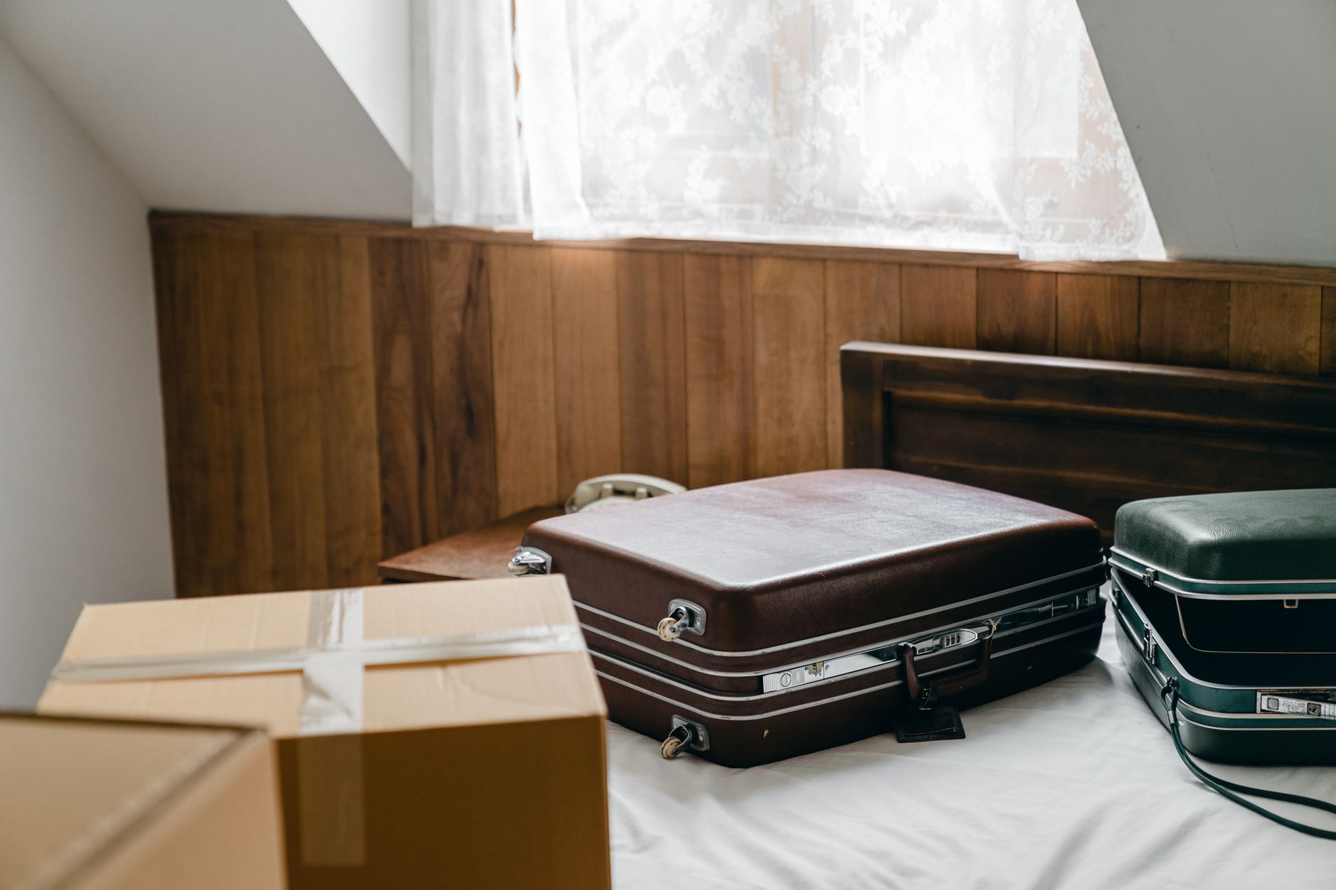 Brown and green suitcases and packed boxes on a bed while preparing for an extended trip