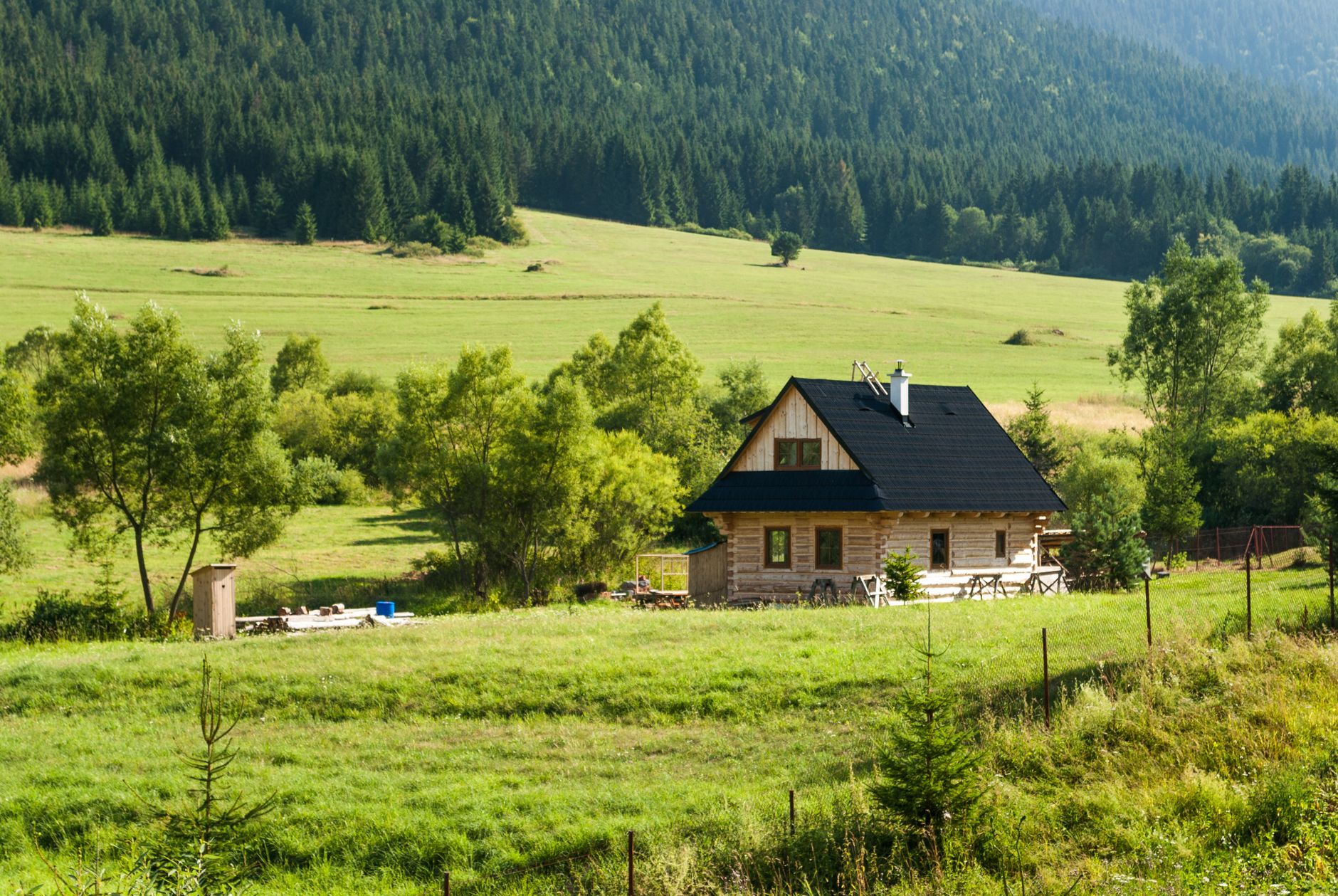 Scenic view of a wooden country house surrounded by lush green fields in Slovakia's countryside.