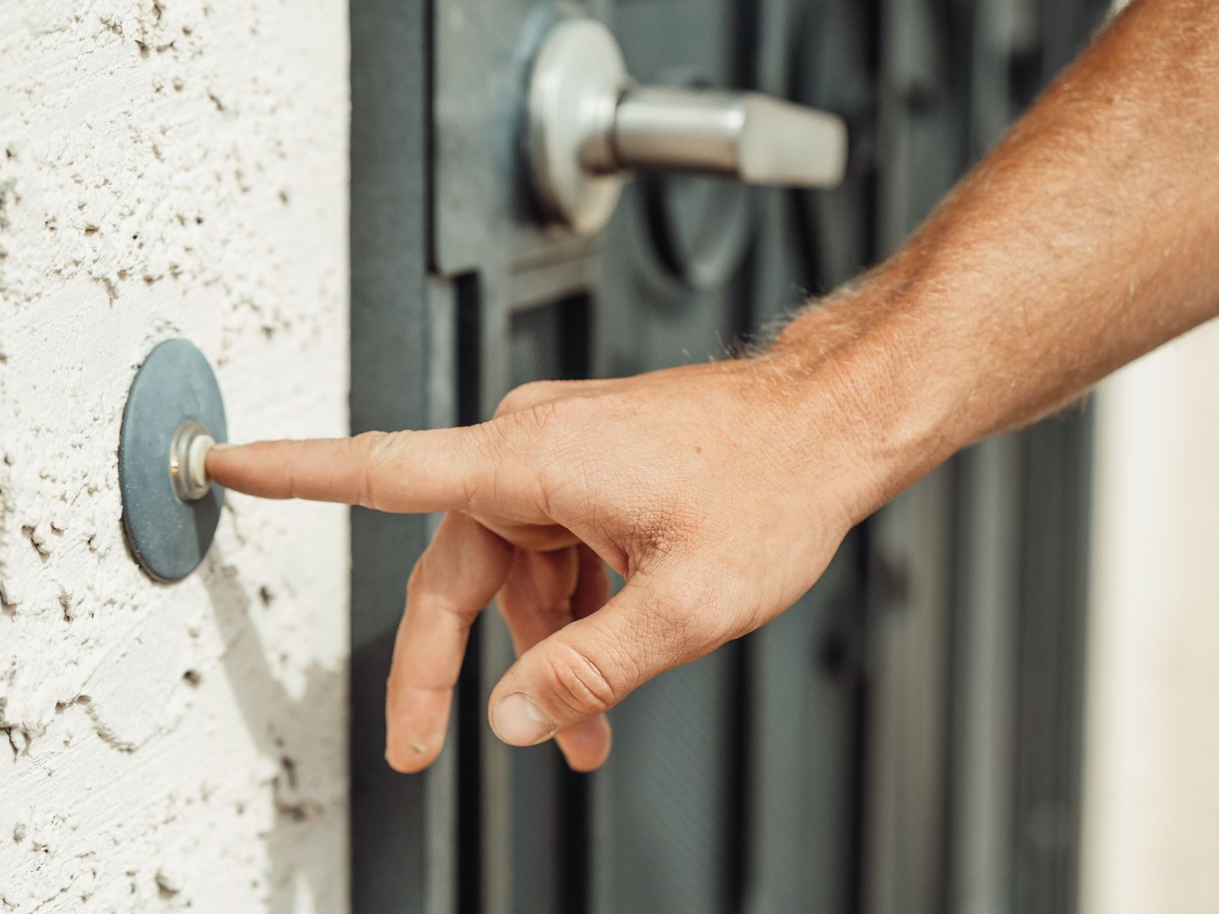 A hand pressing a modern doorbell outside a residential door.