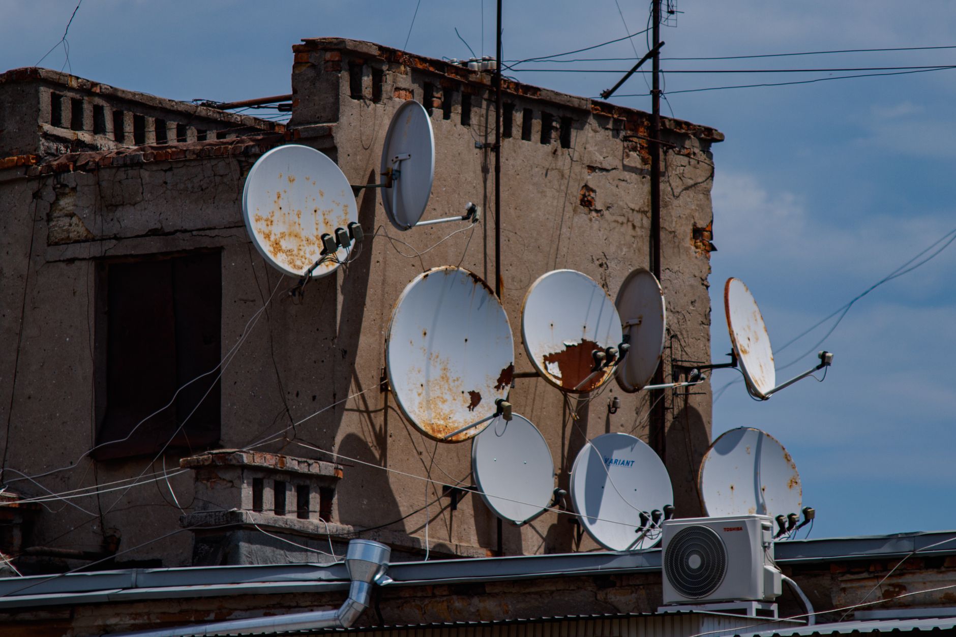 A collection of rusty satellite dishes mounted on an old urban building rooftop.